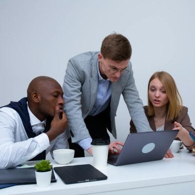 Three colleagues engaged in teamwork around a laptop in a modern office setting.