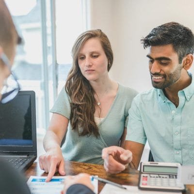 Young couple consulting with a financial advisor using a calculator and documents in a bright office setting.